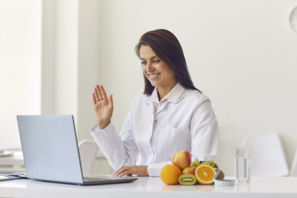 Dietista-Nutricionista genética sonriendo con portátil saludando