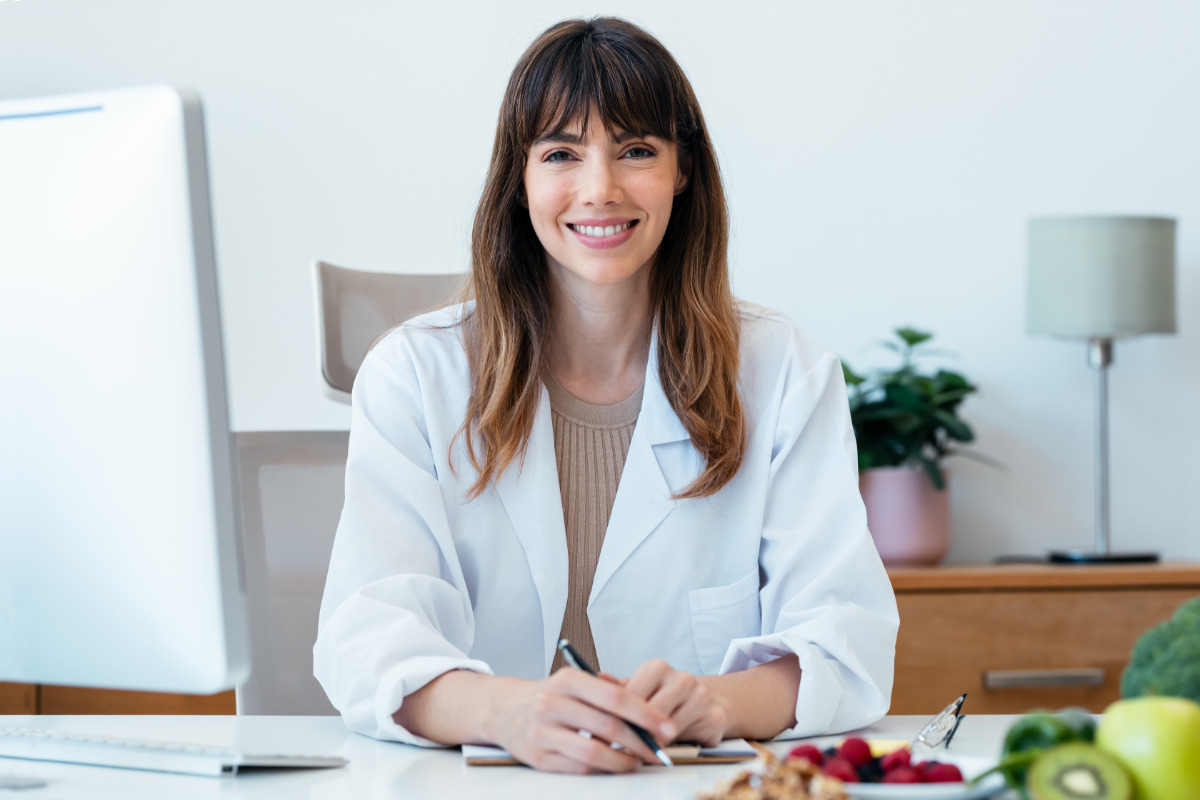 Dietista-Nutricionista-genética-sonriendo-con-ordenador-sentada Dietista-Nutricionista genética sonriendo con ordenador sentada